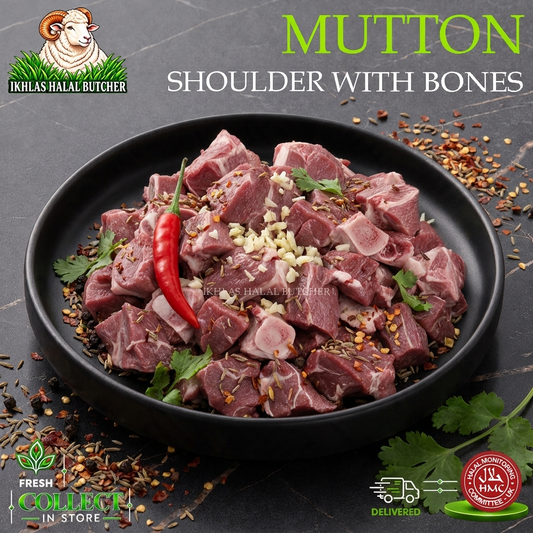 Raw mutton shoulder with bones cut into cubes, presented in a black bowl on a dark stone surface. The meat is garnished with a red chili pepper, minced garlic, and herbs, with scattered spices around it.